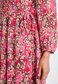 Pink floral dress featuring a textured fabric with a ribbed pattern, long sleeves, and a waist tie for adjustment.
