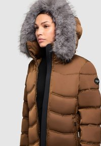 Rjava puhasta jakna s snemljivo sivo krzneno kapuco, prešita tekstura in črni zadržni poudarki. Na levi rokavu je znak.