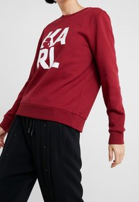 Röd bomullströja med vit logoprint "KARL" på framsidan. Ribbad rundhalsning och manschetter, avslappnad passform, parat med svarta byxor.