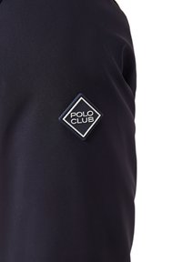 Navy blue jacket with ribbed texture, featuring a diamond-shaped "POLO CLUB" patch on left sleeve. Smooth fabric with minimal design.