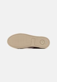 Suola di scarpa in gomma beige chiaro con motivo di grip testurizzato, caratterizzata da un'impronta circolare del logo e bordi lisci.