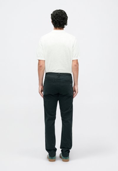 Vyrų apranga, kurioje yra lengvas, kreminės spalvos trumpas rankovėmis marškiniai ir tamsiai žali, tiesūs kelnes su užpakalinėmis kišenėmis ir glotnia tekstūra.