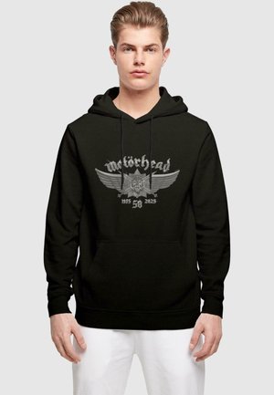 Sort hættetrøje lavet af bomuldsblanding med en grå grafisk design af et skelet og vinger, med teksten "Motörhead 1955 58 2025" nedenfor.