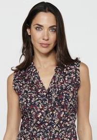 Blusa floreale con sfondo navy, maniche corte, chiusura frontale con bottoni, caratterizzata da piccoli motivi floreali colorati e dettaglio del colletto a volant.