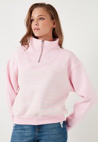 Felpa rosa con mezza zip, colletto alto e strisce orizzontali crema sul petto. Tessuto morbido con polsini e fondo a costine.