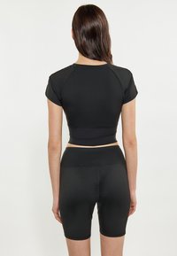 Fekete, testhez simuló, rövid ujjú crop top, magas derekú fekete kerékpáros nadrággal párosítva, sima, rugalmas anyagból. Nincs minta vagy fém díszítés.