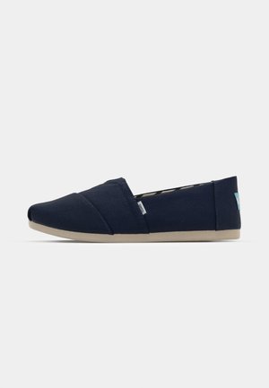 Bottine bleu marine sans lacets en toile avec une texture lisse, dotée d'un bout arrondi, d'une bande élastique et d'une semelle en caoutchouc de couleur claire.
