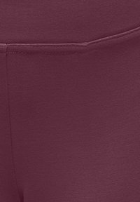 Burgunderfargede leggings med teksturert, elastisk stoff. Har rene linjer og en glatt midjebånd, egnet for aktiv bruk eller uformell bruk.