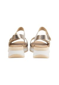 Sandalias strappy metálicas doradas con una plantilla acolchada beige y un tacón blanco en bloque. Correas texturizadas y detalle de cierre ajustable.