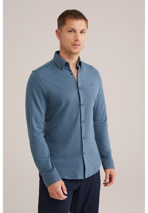 Camisa de manga larga abotonada en azul oscuro. Tejido suave con una ligera textura, que presenta un cuello abotonado y un logo sutil en el pecho.