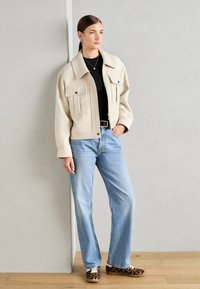 Beige zkrácená bunda se dvěma předními kapsami, spárovaná s světle modrými džíny rovného střihu a botami s leopardím vzorem. Hladká tkanina, uvolněný střih.