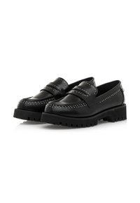 Une paire de mocassins en cuir noir avec des détails cloutés et des semelles en caoutchouc épaisses, présentée sur un fond blanc.