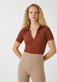 Braun gestreifter kurzärmeliger Oberteil mit tiefem V-Ausschnitt und Kragen, kombiniert mit hochtaillierten gemusterten Hosen mit einem Karodesign in Beige und Braun.