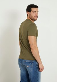 Olivengrønt tætsiddende t-shirt med korte ærmer, blød tekstur og rund halsudskæring, parret med blå afblegede jeans med et patchlogo.