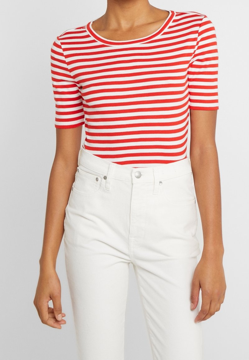 Top de manga corta a rayas rojas y blancas con cuello redondo, combinado con jeans blancos de cintura alta. Textura suave, diseño ajustado.