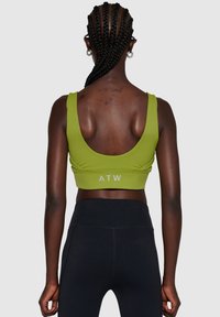 Grøn sports-bh med scoop ryg, der har et "ATW" logo ved sømmen. Glat, strækbart stof parret med sorte, højtaljede leggings.