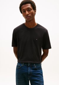 Črna bombažna majica z okroglim izrezom in kratkimi rokavi. Na prsih majhen prepoznaven logotip. Kombinirana z modrimi jeans hlačami.