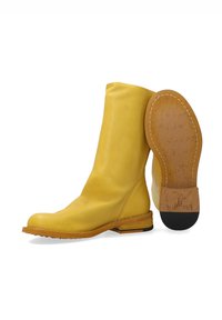 Gule læder ankelstøvler med en glat tekstur, rund tå og en stablet hæl. Sålen er brun med en struktureret finish.