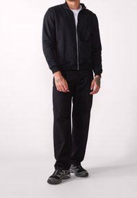 Giacca nera con zip e colletto alto, abbinata a pantaloni neri e scarpe sportive. Caratterizzata da un design elegante e una silhouette aderente.
