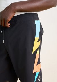 Shorts de bain noirs avec un motif d'éclairs multicolores en bleu, jaune, orange et rose, dotés d'une taille à cordon et d'une poche latérale.