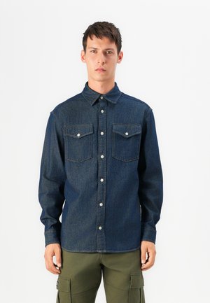 Camicia in denim blu scuro con colletto button-down, due tasche sul petto e bottoni bianchi; maniche lunghe con polsini abbottonati.