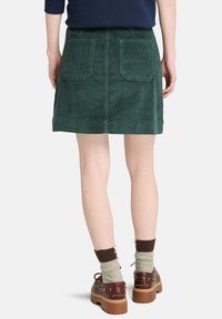 Groene corduroy A-lijn rok met twee vlakke achterzakken, met een gestructureerd ribbeloppervlak. Gemaakt met bruine schoenen en een patroon op de sokken.