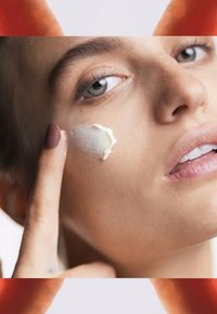 Crème hydratante appliquée sur une peau claire avec un doigt. Texture lisse et blanche visible sur la joue. Détails subtils en arrière-plan.