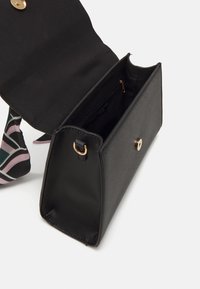 Bolso de mano rectangular negro con superficie texturizada, herrajes dorados y un bolsillo interior con cremallera. Presenta una correa con un diseño visible en su interior.