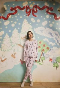 Růžová pyžamová souprava se hravými ilustracemi postav, jelenů a zimních scén. Měkká tkanina s dlouhými rukávy a elastickými manžetami na kalhotách.