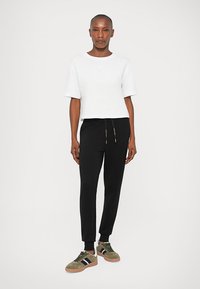 White cropped t-shirt with short sleeves, paired with black tapered sweatpants featuring a drawstring waist, and green sneakers with black stripes.
