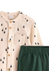 Lichtbeige shirt met zwarte boommotieven en houten knopen, gecombineerd met donkergroene broek met elastische tailleband, van katoenmix materiaal.