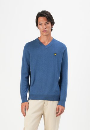Pull bleu en V en tissu tricoté avec des manches longues et des bords côtes, arborant un petit logo jaune sur la poitrine gauche.