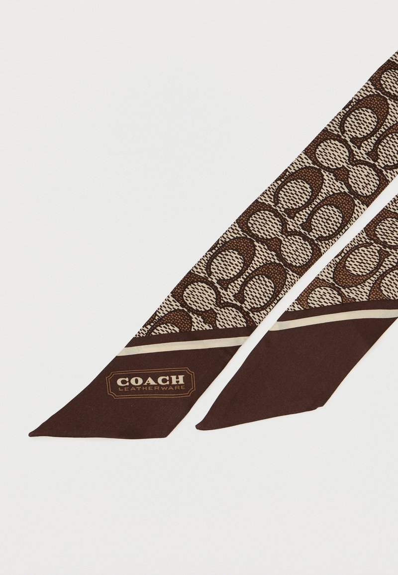 Bruine zijden sjaal met een gepattern ontwerp in crème en donkerbruin. Het ene uiteinde toont het gouden "COACH" logo en een effen donkerbruin accent.