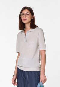 Lichtgrijs poloshirt met korte mouwen, kraag, vier knopen en geborduurde bloemenmotieven aan de voorkant. Zacht brei-textuur.
