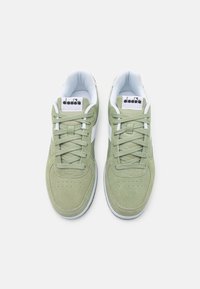 Zelené semišové tenisky s bílými akcenty, charakterizované hladkou strukturou, perforovanou špičkou a zaobleným tvarem. Šněrovány zelenými tkaničkami ve stejném odstínu.