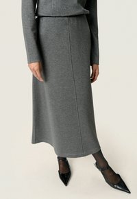 Gonna midi grigia a maglia con design dritto, caratterizzata da un delicato dettaglio di cucitura, abbinata a tacchi a punta neri e collant neri trasparenti.