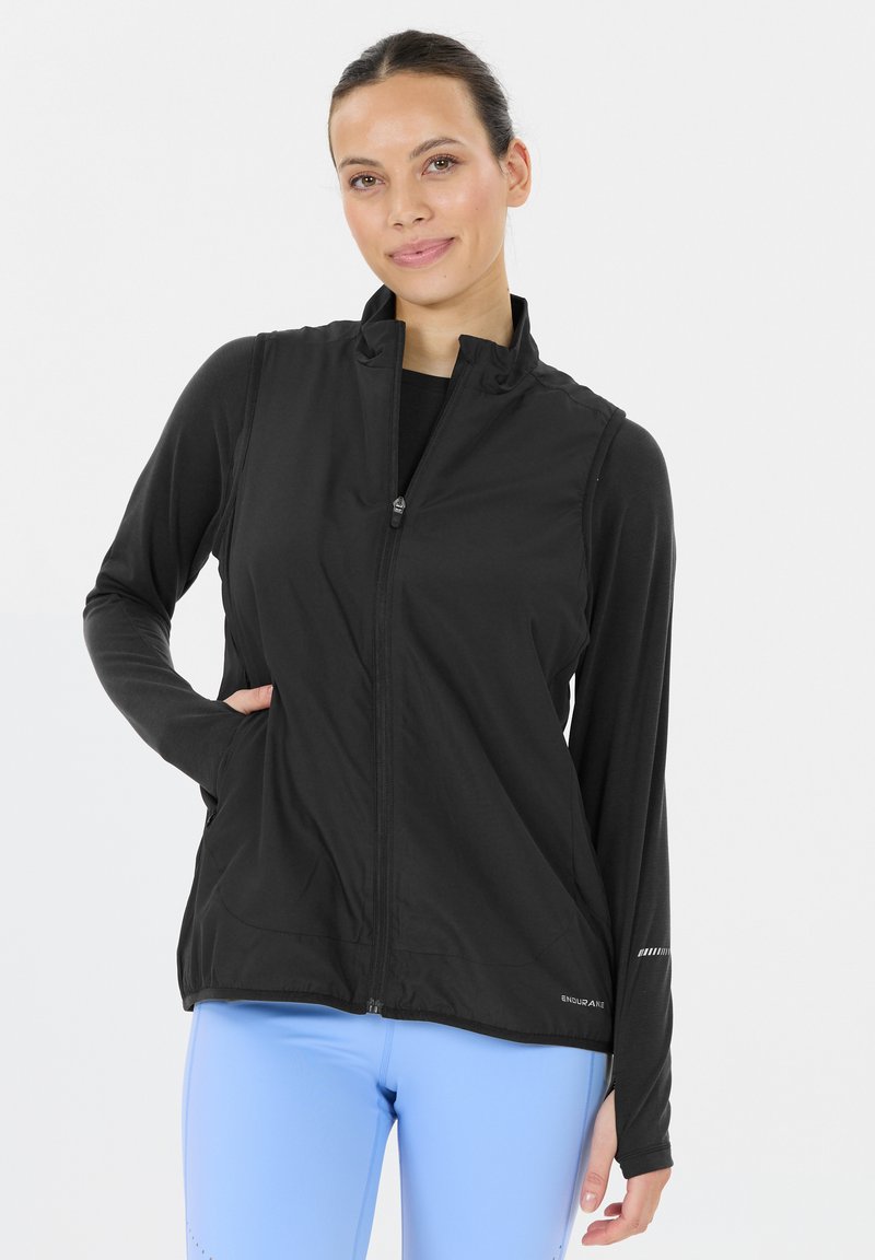 Svart atletisk väst med dragkedja, hög krage och två sidofickor. Slät struktur med reflekterande detaljer på ärmar och nederkant.