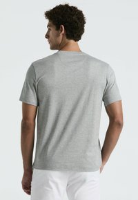 T-shirt gris à manches courtes en tissu doux, avec un col rond et une coupe décontractée. Le dos présente une texture lisse avec un minimum de détails.