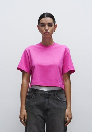 Top corto di colore rosa acceso con maniche corte e scollatura rotonda, abbinato a jeans in denim grigio scuro a vita alta. Texture liscia.