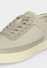 Baskets Calvin Klein beige clair avec lacets en tissu et détails en daim, avec une semelle blanche texturée.