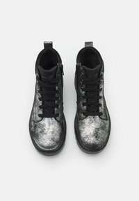 Sorte joggesko med en metallisk sølvfinish, snøring og teksturert overflate. Har en svart stoffforing og etikett på tungen.