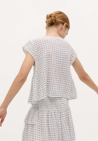 Haut blanc fluide à manches courtes, orné d'un motif répété rouge et bleu. Taille froncée avec un style peplum. Tissu doux et léger.