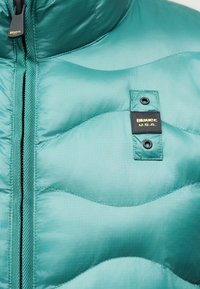 Veste matelassée turquoise avec fermeture éclair noire et étiquette noire cousue sur la poitrine portant l'inscription "Blauer U.S.A."