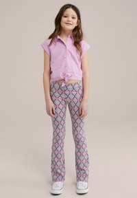 Rosa īsās piedurknes pogājamā krekla, kas savilkts jostasvietā, kombinācija ar rakstainiem platiem biksēm purpura, zila un baltos dimanta formas, baltas sporta kurpes.