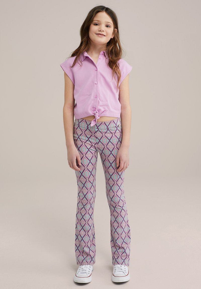 Rosa īsās piedurknes pogājamā krekla, kas savilkts jostasvietā, kombinācija ar rakstainiem platiem biksēm purpura, zila un baltos dimanta formas, baltas sporta kurpes.