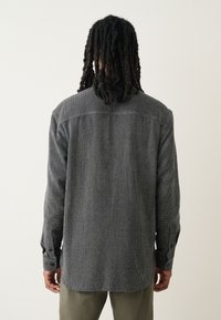 Camisa con estampado en blanco y negro, cuello abotonado, mangas largas y dobladillo recto, confeccionada en tela texturizada.