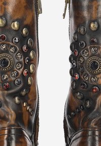 Braune Lederstiefel mit dekorativen Metallnieten und Edelsteinen, ausgestattet mit einem Reißverschluss an der Seite und kunstvollen runden Mustern am Schaft.