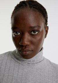 Grauer, gerippter Rollkragenpullover mit hohem Kragen; Nahaufnahme eines Gesichts mit glatter Haut und markanten, hellen Augen.