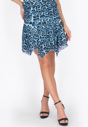 Blauw-zwarte sjaalrok met luipaardprint, gedragen met zwarte enkellaarzen met bandje, gekruiste benen zichtbaar tegen een witte achtergrond.