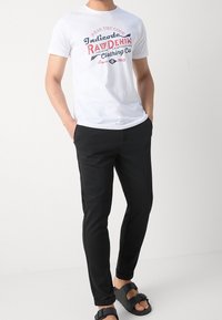 Biała bawełniana koszulka z grafika w czerwonym i niebieskim kolorze, zestawiona z czarnymi slim-fit spodniami oraz czarnymi klapkami z detalem klamry.